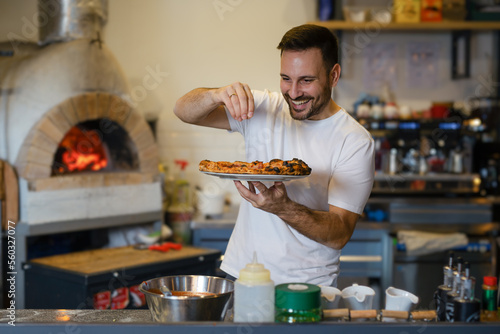 Fototapet Male chef is sprinkling fresh oregano over a traditionally made home pizza