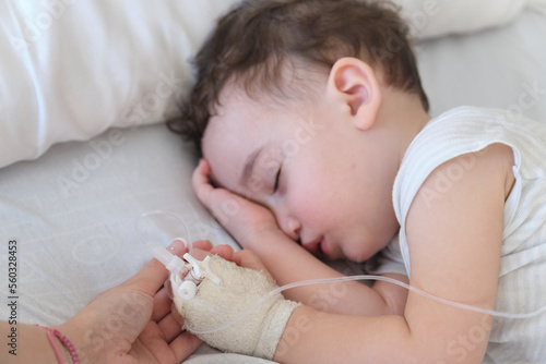 sick toddler in hospital holding mother's hand while sleeping