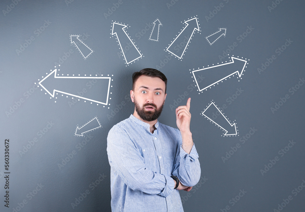 Choice in profession or other areas of life, concept. Making decision, emotional man surrounded by drawn arrows on grey background Choice in profession or other areas of life, concept. Making decision, emotional man surrounded by drawn arrows on grey background