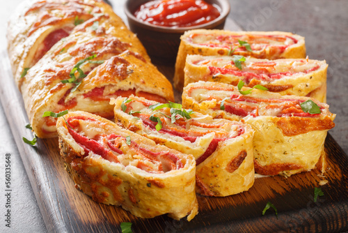 Italian food Pizza roll stromboli with cheese, salami and tomatoes closeup on the wooden board on the table. Horizontal