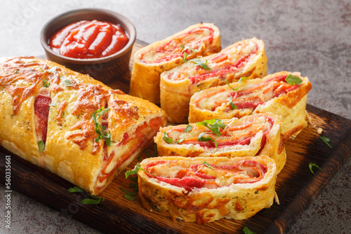 Delicious pizza stromboli roll stuffed with salami sausage and mozzarella cheese close-up on a wooden board on the table. horizontal photo