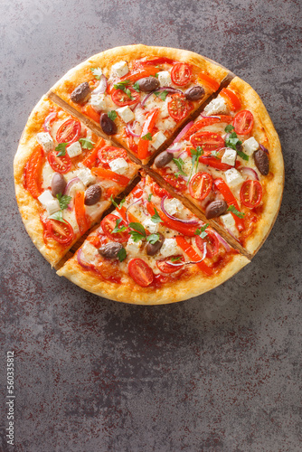 Vegetarian Greek pizza with peppers, feta, onions, tomatoes, olives and herbs close-up on a wooden board on the table. Vertical top view from above