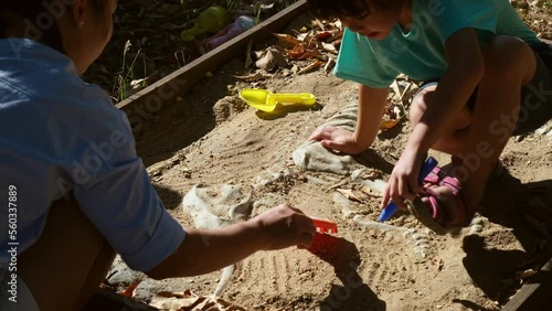 Cute little girl playing as a little archaeologist with her mother digging dinosaur fossils in the playground. Children learning about, Excavating dinosaur fossils simulation in the park.