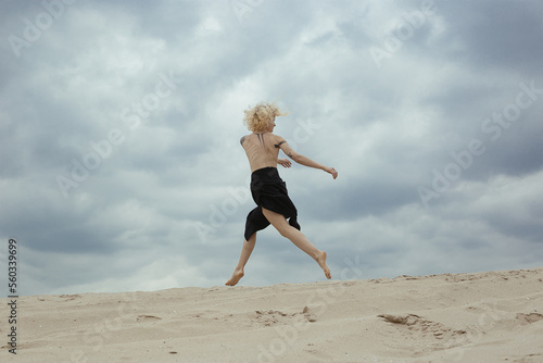 Elegant bare woman jumping on beach scenic photography. Picture of person with overcast sky on background. High quality wallpaper. Photo concept for ads, travel blog, magazine, article
