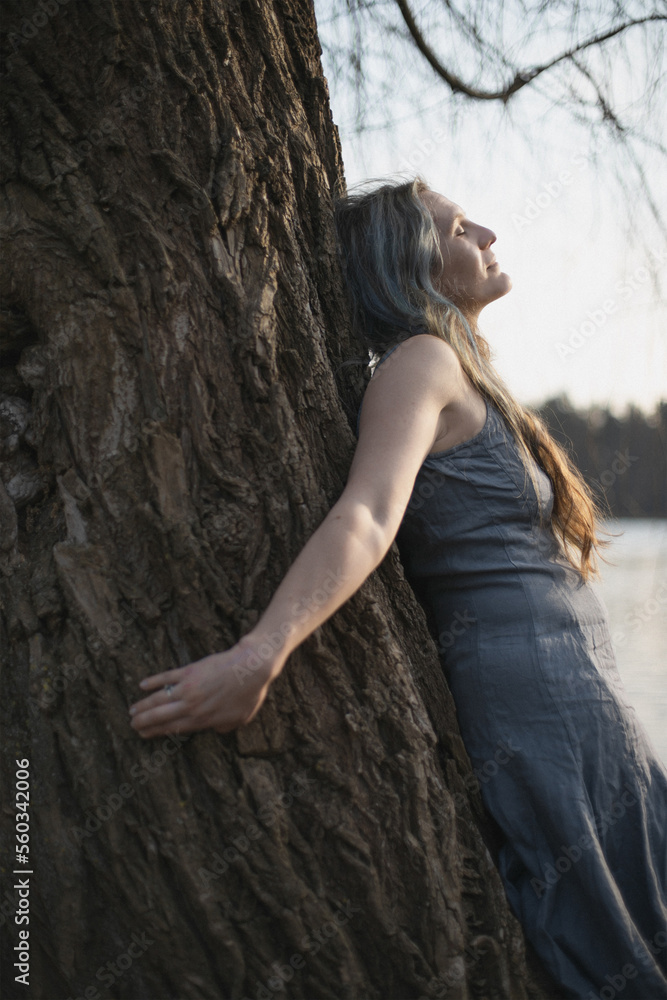 Close up woman spiritually connecting with willow tree portrait picture. Healing. Closeup side view photography with blurred background. High quality photo for ads, travel blog, magazine, article Close up woman spiritually connecting with willow tree portrait picture. Healing. Closeup side view photography with blurred background. High quality photo for ads, travel blog, magazine, article