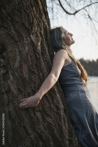 Close up woman spiritually connecting with willow tree portrait picture. Healing. Closeup side view photography with blurred background. High quality photo for ads, travel blog, magazine, article