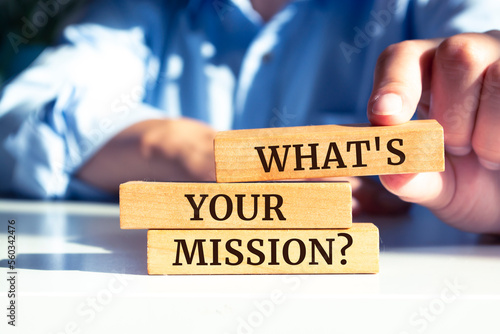 Closeup on businessman holding a wooden block with "What's your mission?" message, business concept