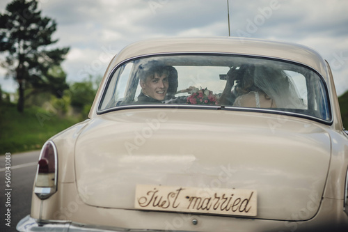 Photography Happy bride and groom, newlywed wedding couple is sitting in a retro car on a country road for honeymoon after the ceremony