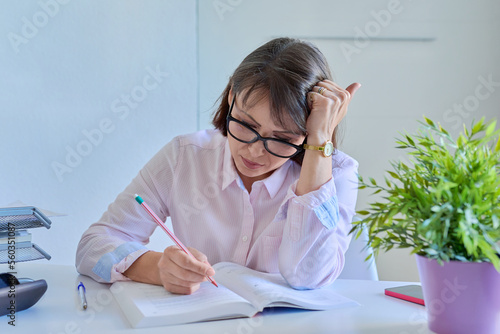 Middle-aged female working at home at table with books