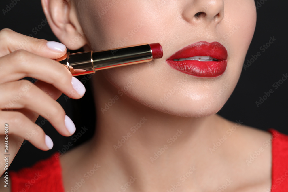 Young woman with beautiful makeup holding red lipstick on black background, closeup