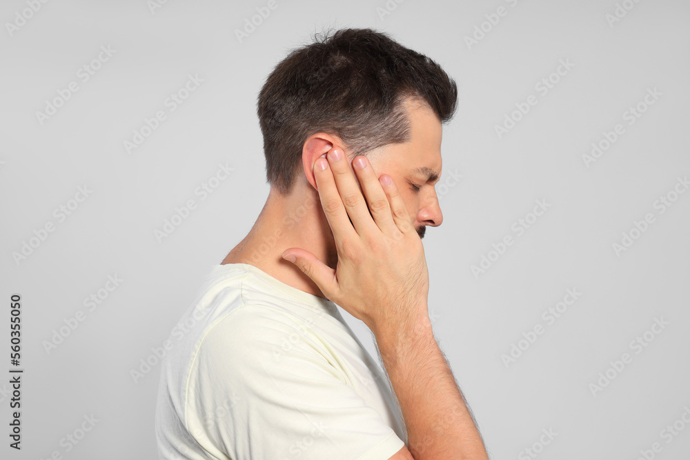 Man suffering from ear pain on grey background Man suffering from ear pain on grey background