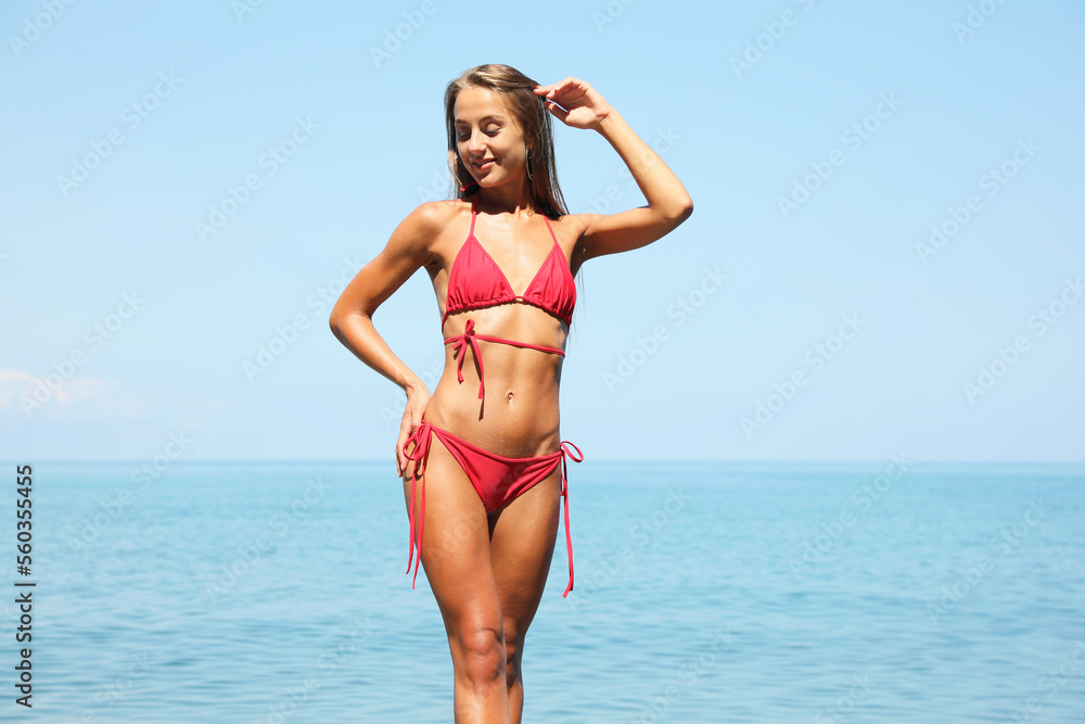 Beautiful young woman in stylish bikini on seashore, space for text