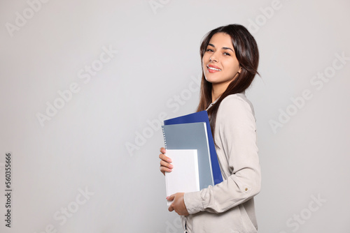 Happy young teacher with books on light grey background. Space for text