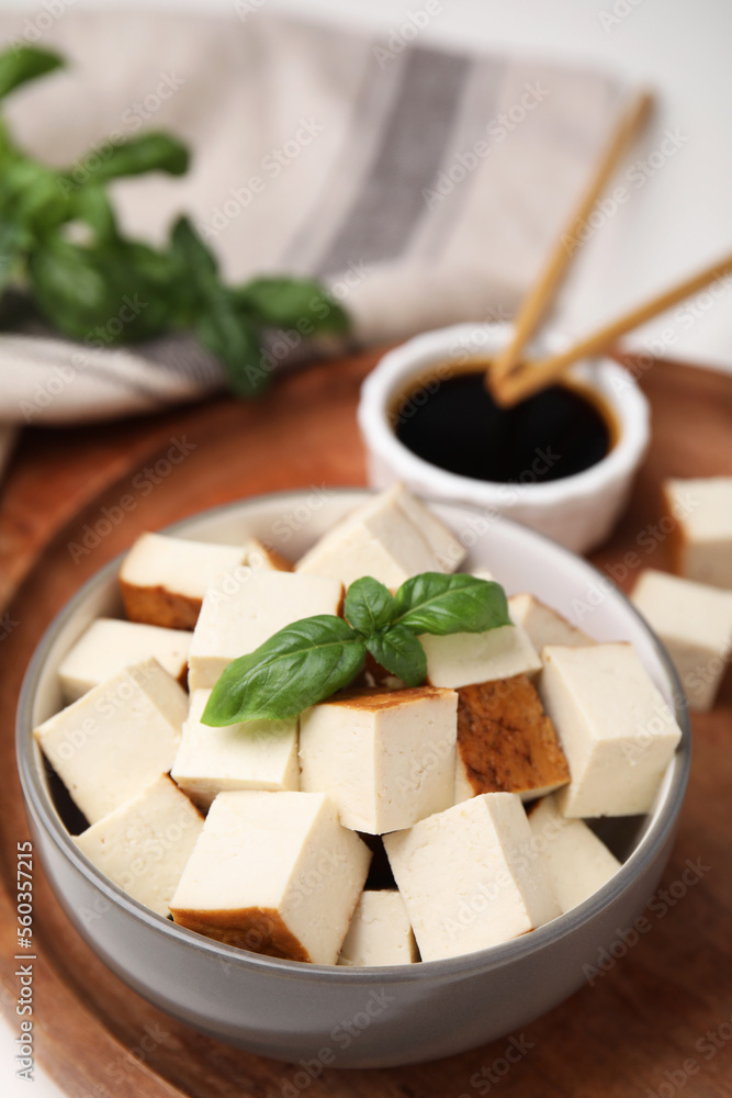 Bowl of smoked tofu cubes, soy sauce and basil on wooden tray, closeup