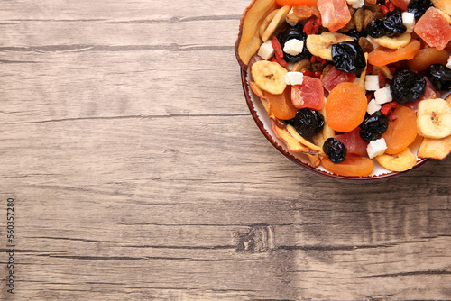 Bowl with different tasty dried fruits on wooden table, top view. Space for text