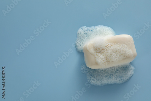Soap bar with fluffy foam on light blue background, top view. Space for text