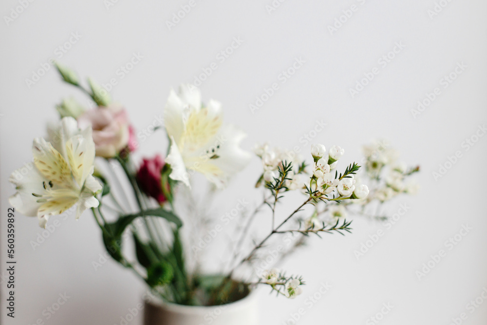 Stylish bouquet in ceramic vase at window, moody image. Beautiful fresh flowers, manuka, alstroemeria, eustoma, eucalyptus floral arrangement. Spring modern bouquet close up - obrazy, fototapety, plakaty 