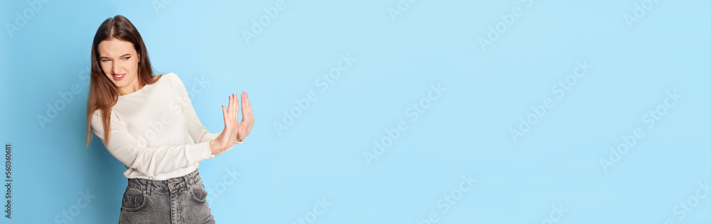 Rejection, refusing. Portrait of young beautiful girl in casual clothes posing over blue studio background. Banner, flyer. Concept of emotions, lifestyle, youth Rejection, refusing. Portrait of young beautiful girl in casual clothes posing over blue studio background. Banner, flyer. Concept of emotions, lifestyle, youth
