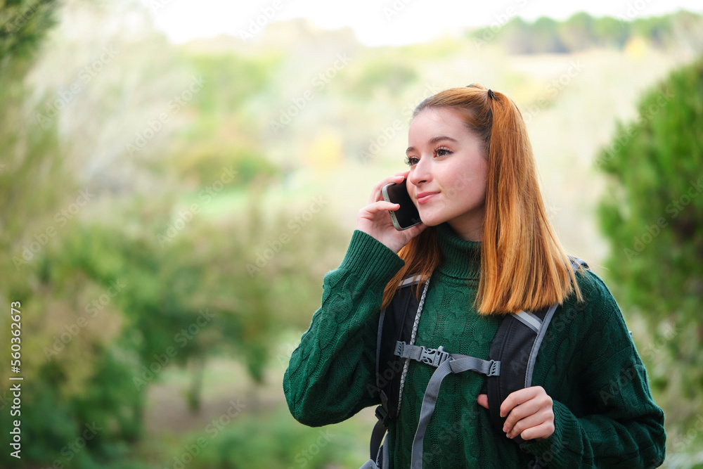 Happy redhead young female hiker talking on phone while trekking. Hiking concept. Happy redhead young female hiker talking on phone while trekking. Hiking concept.