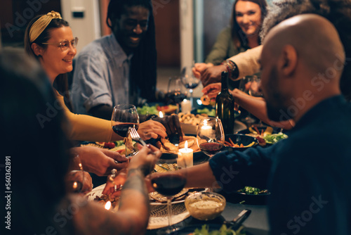 multiethnic people sitting together in a joyful night at home or restaurant eating vegetarian food and drinking wine celebrating friendship and family life
