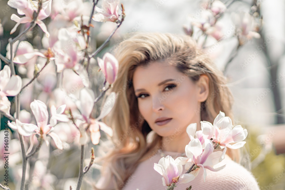 Fototapeta premium Portrait of a beautiful happy middle aged woman enjoying the smell in a blooming spring garden. Beautiful magnolia bushes, large flowers.