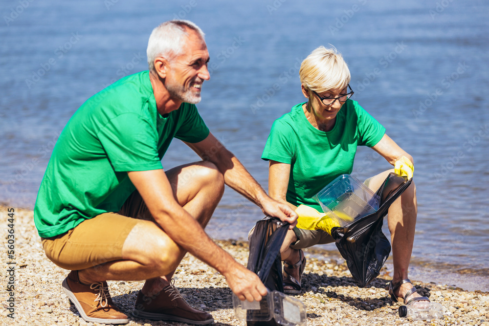 Mature volunteers gathering garbage on the sea coast. Ecology concept Mature volunteers gathering garbage on the sea coast. Ecology concept