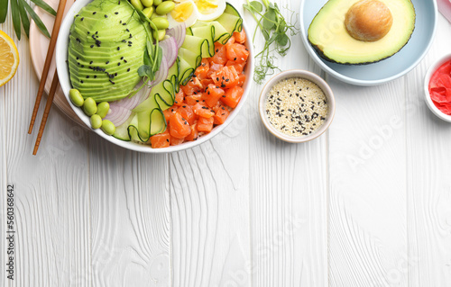 Delicious poke bowl with avocado, fish and edamame beans on white wooden table, flat lay. Space for text