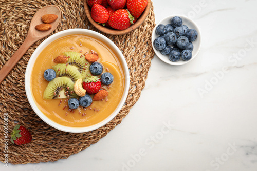 Delicious smoothie bowl with fresh berries, kiwi and nuts on white table, flat lay. Space for text