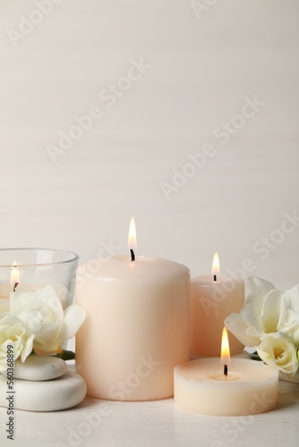 Beautiful composition with burning candles, spa stones and flowers on white table. Space for text