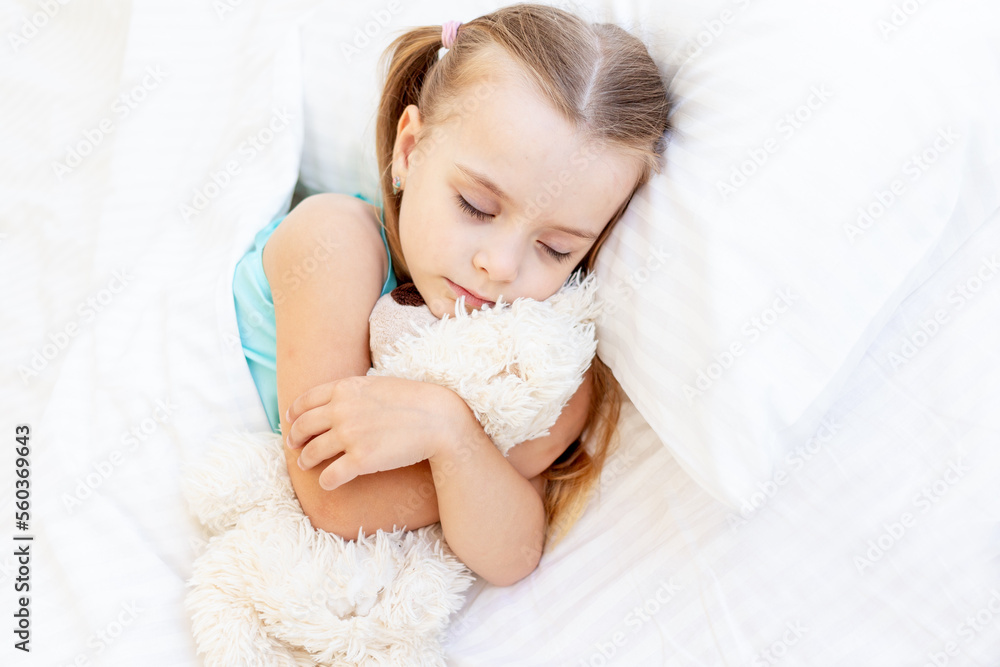 a girl child is sleeping on a bed at home on a white cotton bed hugging a teddy bear toy in her hands and smiling sweetly in her sleep a girl child is sleeping on a bed at home on a white cotton bed hugging a teddy bear toy in her hands and smiling sweetly in her sleep