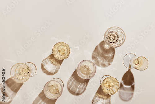Summer party drinks flat lay, wine glasses with white sparkling wine and sunshine shadow on light table. Minimal pattern with beautiful wine glasses, above view still life, beige golden color photo