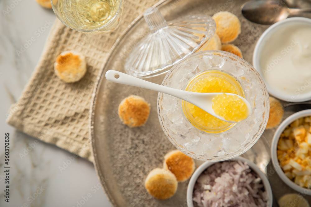 Gelber Saiblings Kaviar auf Eis in Glas Schale mit Porzellan Löffel, gekochte Eier Würfel, Charlotten Zwiebel Würfel, Toast Brot, Saure Sahne und Champagner Sekt auf Silber Teller und Marmor hell Gelber Saiblings Kaviar auf Eis in Glas Schale mit Porzellan Löffel, gekochte Eier Würfel, Charlotten Zwiebel Würfel, Toast Brot, Saure Sahne und Champagner Sekt auf Silber Teller und Marmor hell