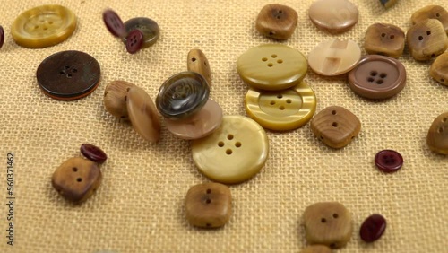 Brown buttons in different designs and sizes for sewing on clothes fall on brown burlap, slow motion photo