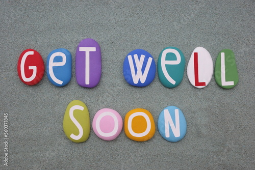 Get well soon, creative message composed with multi colored stone letters over green sand