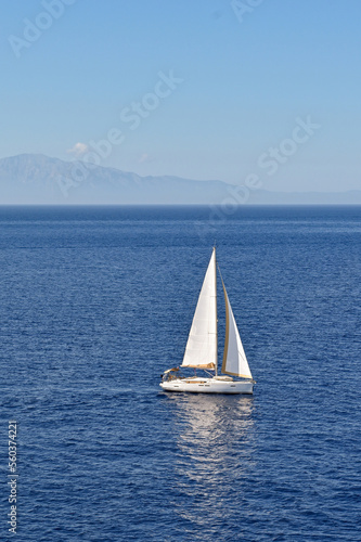 Sailing yacht with white sail on a calm sea with coastline in the background