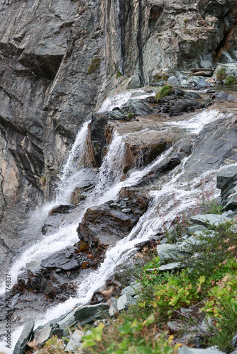 Foaming streams of alpine waterfall shot in contrast and with high sharpness against the background of granite dark rocks overgrown with sparse green vegetation  Aosta valley  Italy