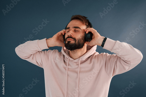 In headphones. Handsome man is in the studio against blue background