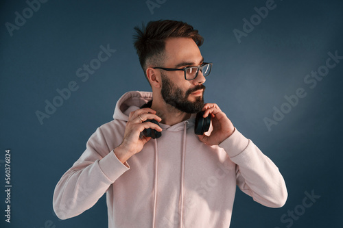 In glasses and with headphones. Handsome man is in the studio against blue background