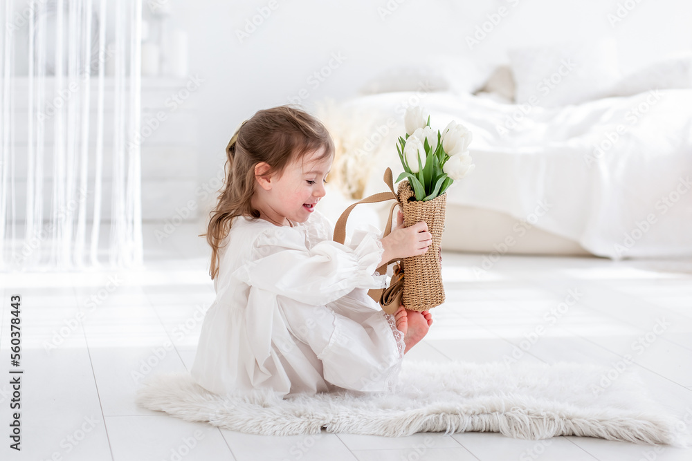 Close-up portrait of a little girl in a white dress, nightgown. Toddler embraces a bouquet of fresh Close-up portrait of a little girl in a white dress, nightgown. Toddler embraces a bouquet of fresh