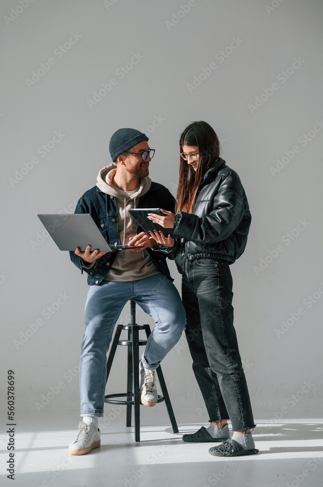 Beautiful man and woman are together in the studio against background. With laptop and tablet in hands