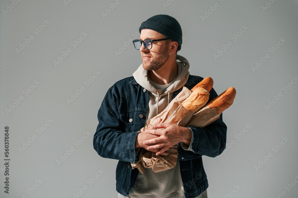 With bunch of baguettes in hands. Handsome man is in the studio against white background With bunch of baguettes in hands. Handsome man is in the studio against white background