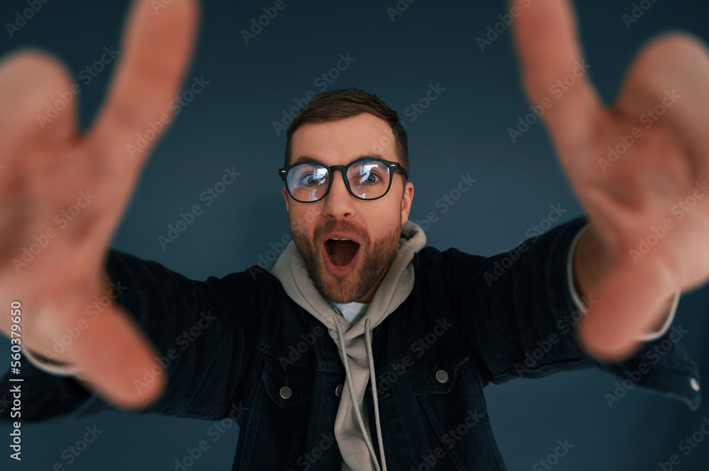 Naklejka premium Guy is pretending that he's doing photoshoot by using hands gestures. Handsome man is in the studio against blue background