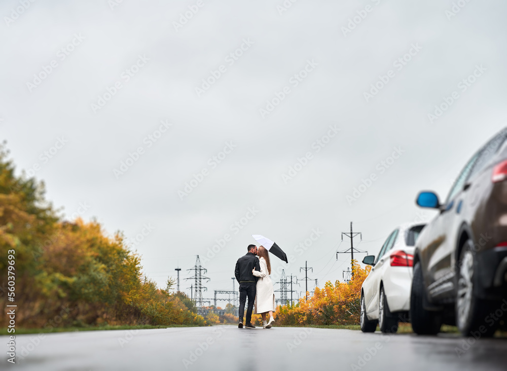 Couple in love on the road near cars under cloudy sky