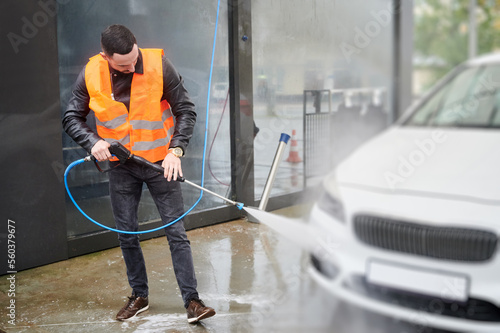 Man washing car on carwash station, wearing orange vest