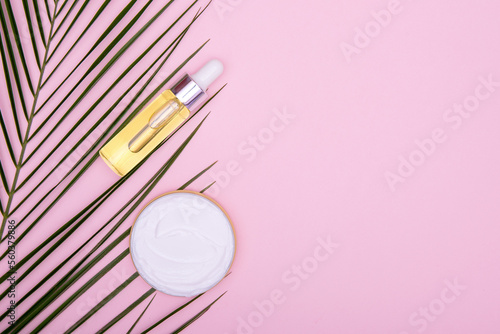 Cosmetic oil, cream and palm leaf on a pink background. The concept of face and body care. Beauty and spa background. copy space