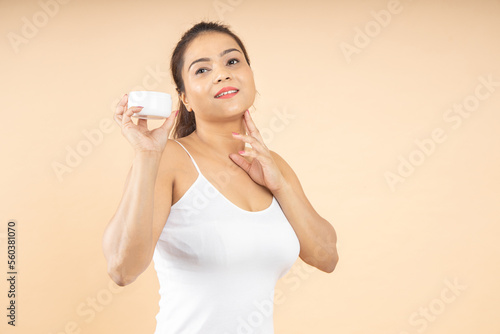Beautiful young indian woman 20s applying moisturizing cream on face. Smiling Asian brunette pretty lady smoothing perfect skin, isolated on beige background studio portrait, Beauty Product. © gajendra