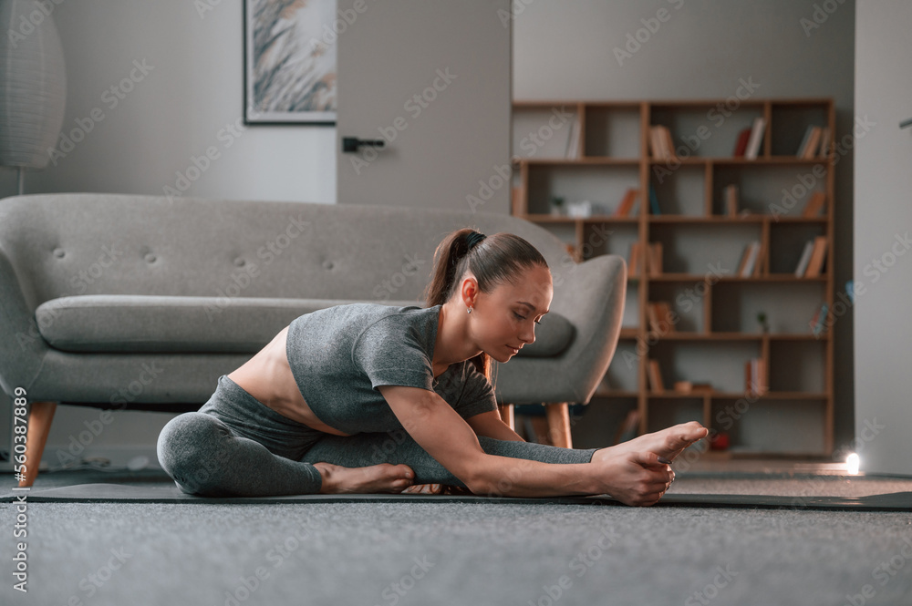 Fototapeta premium In yoga clothes. Doing stretching. Young woman doing fitness indoors
