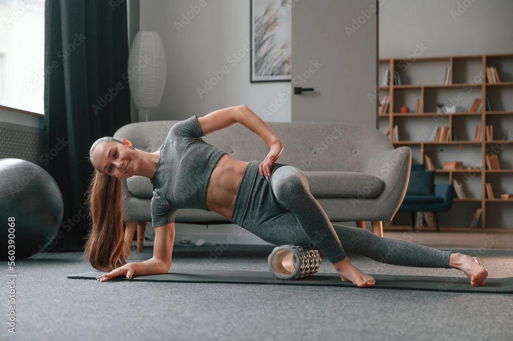 On the right hand and leg on the foam roller. Young woman in yoga clothes doing fitness indoors On the right hand and leg on the foam roller. Young woman in yoga clothes doing fitness indoors