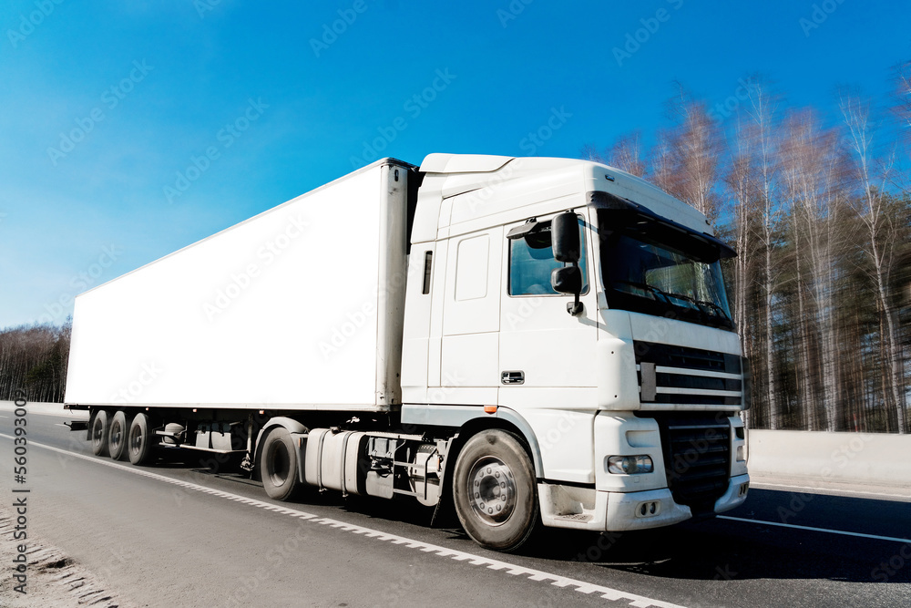 Delivery cargo truck with long empty white trailer driving on highway.