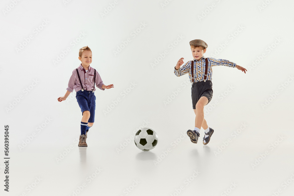 Competition. Boys, children in classical retro clothes playing football over grey studio background. Concept of game, childhood, friendship Competition. Boys, children in classical retro clothes playing football over grey studio background. Concept of game, childhood, friendship